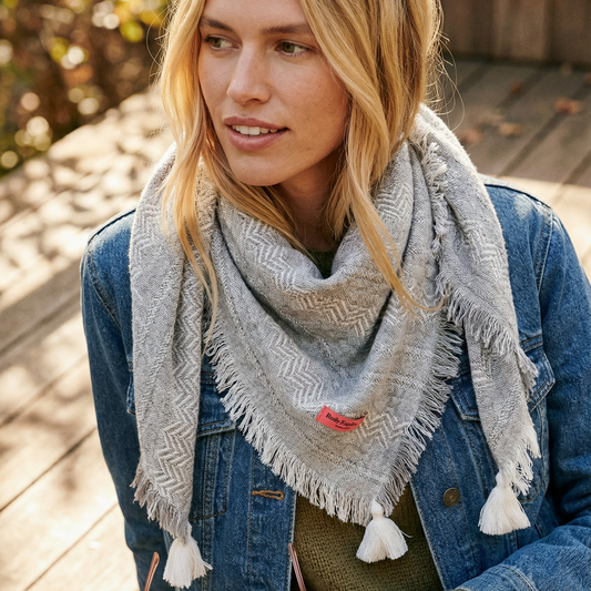 Woman wearing a gray patterned scarf and denim jacket on a wooden deck.
